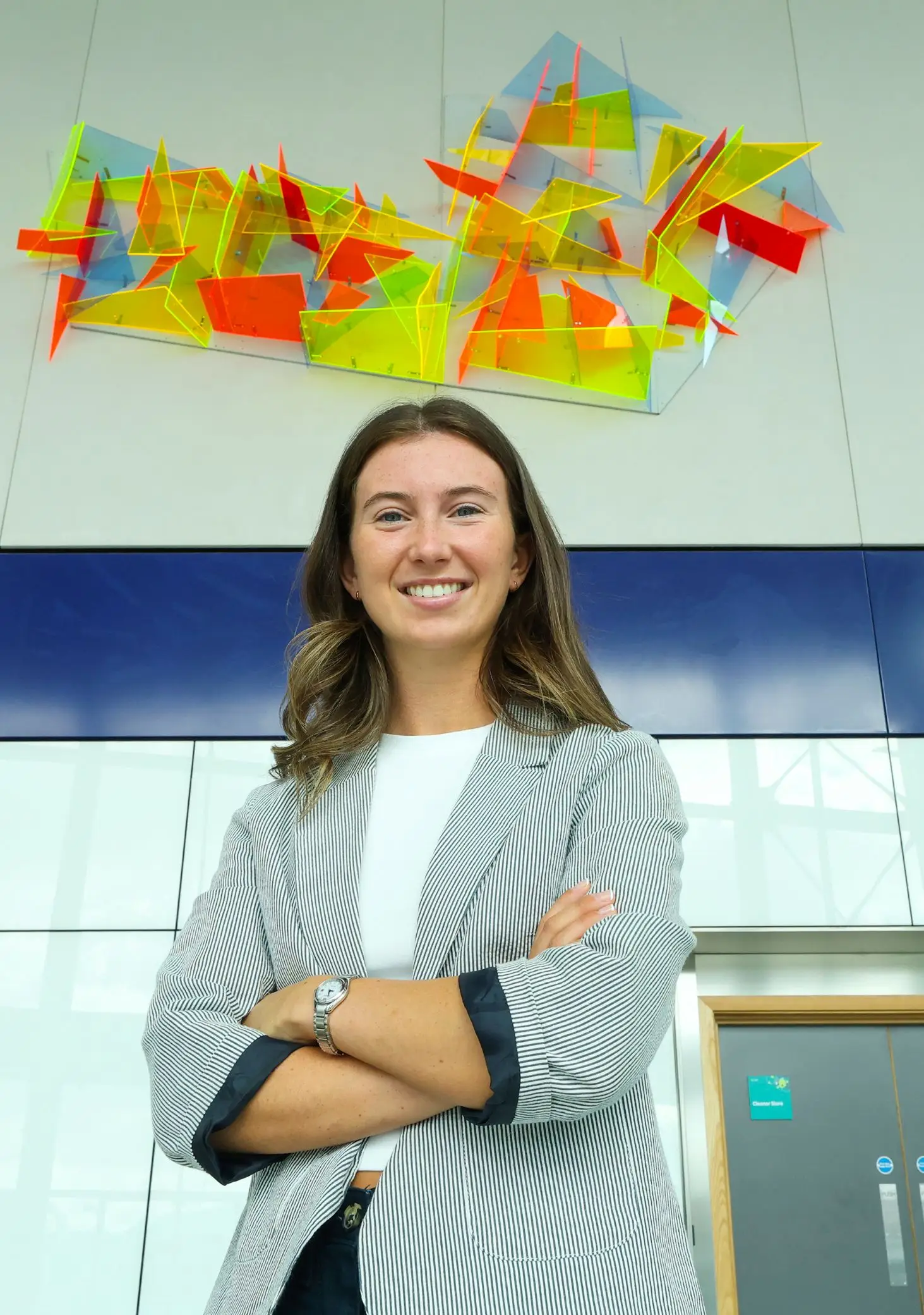 A photograph of artist Hollie Massy in front of her artwork at Belfast Grand Central Station.